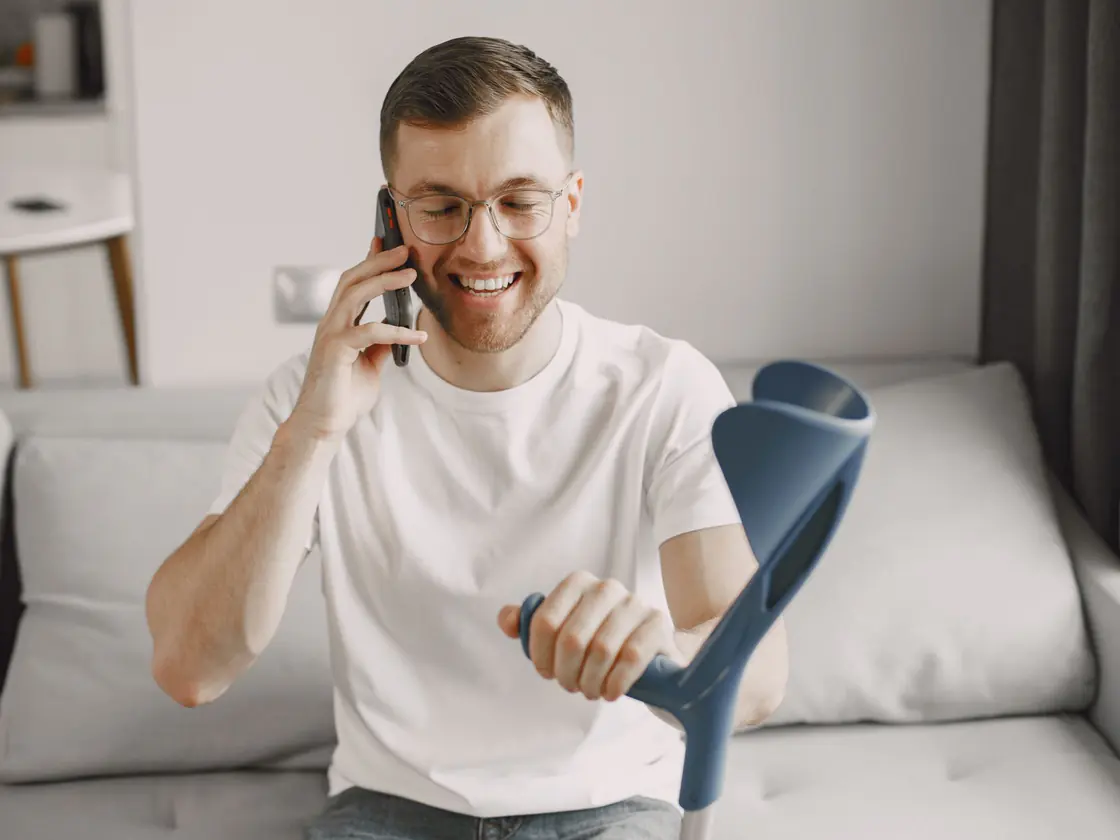 A man recovering at home with a crutch, taking a phone call