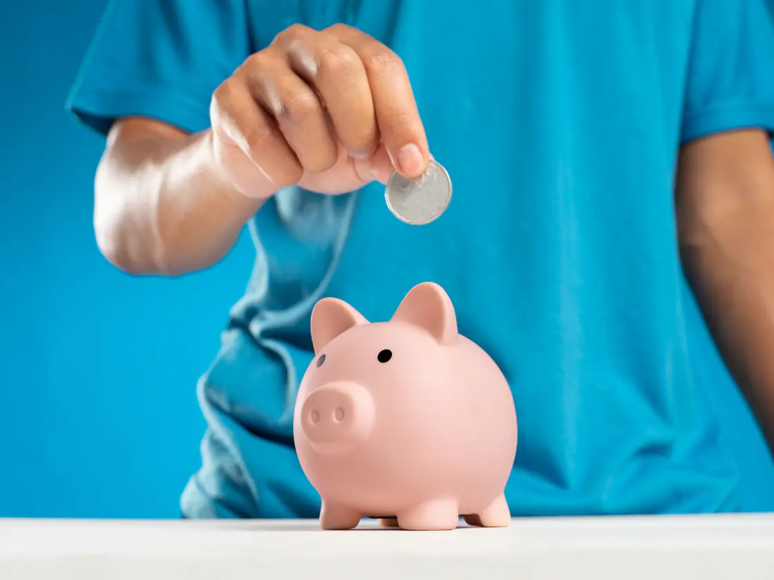 A hand dropping a coin into a piggy bank
