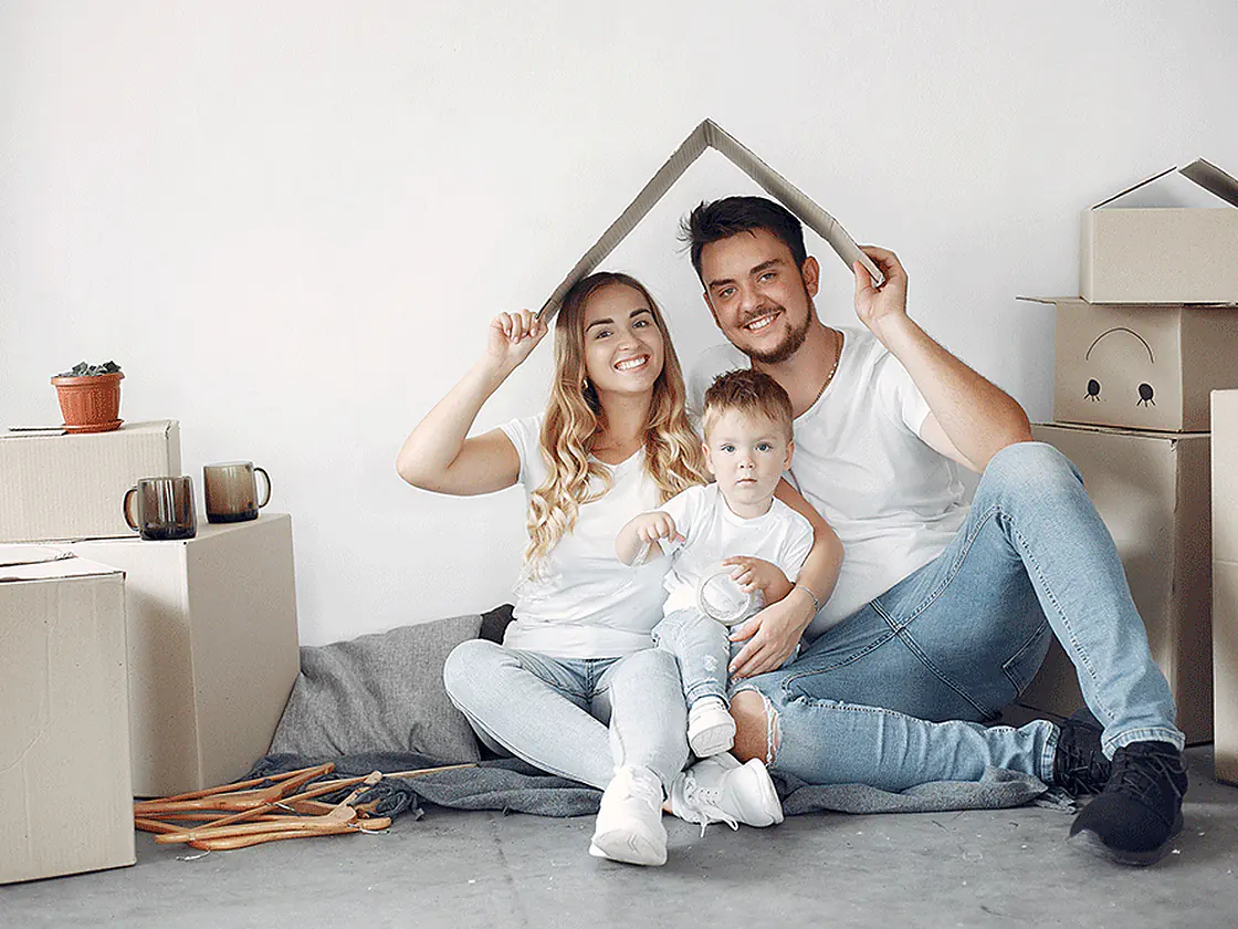 Parents and their child sitting under a cardboard roof in their new home