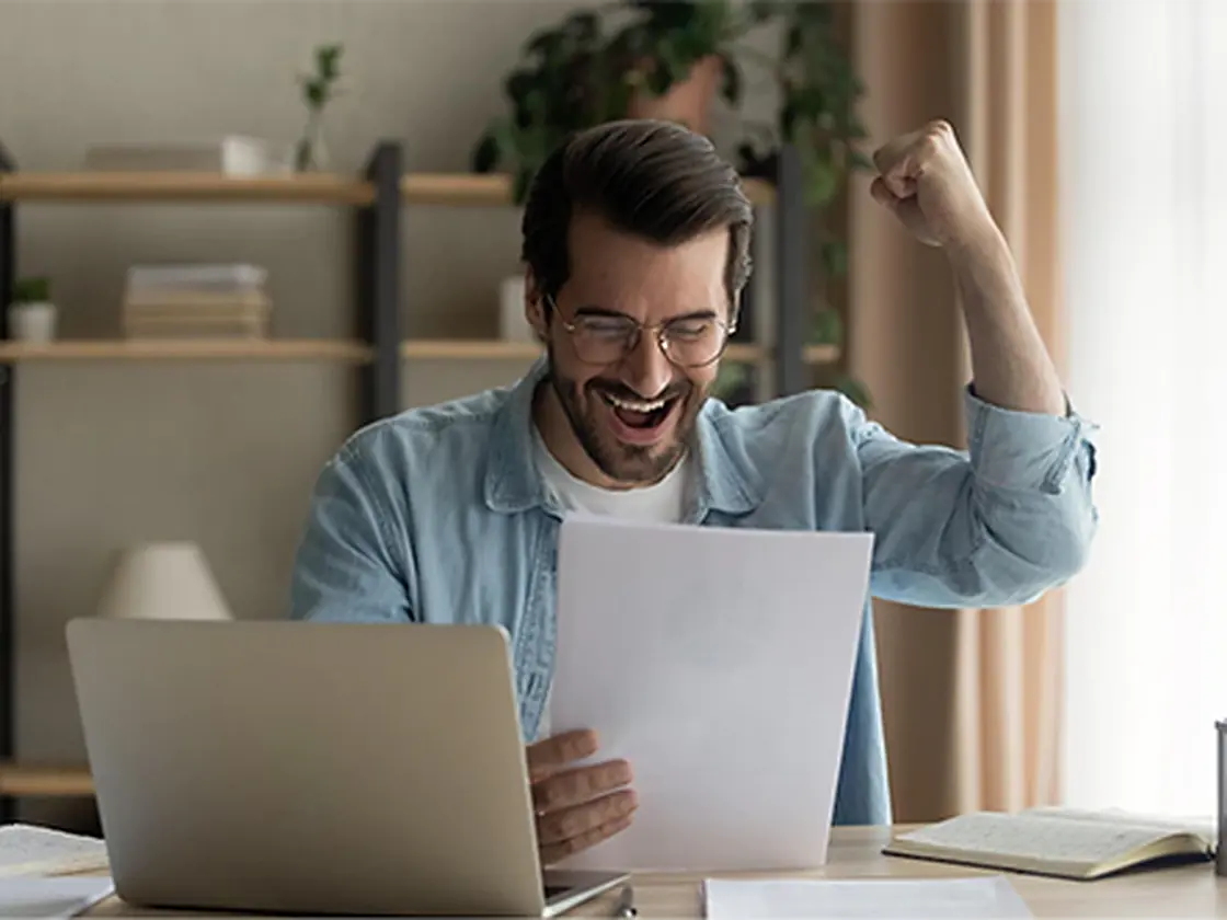 A man celebrating good news while reading a document at his desk