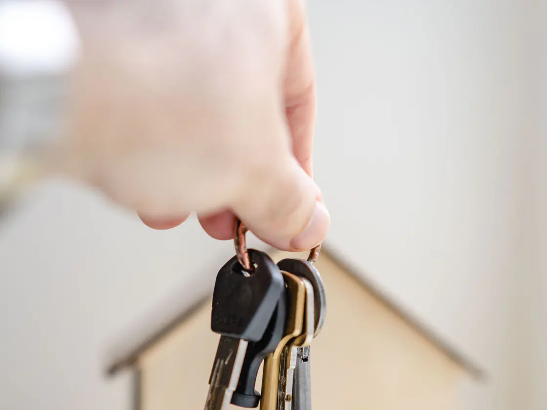 A hand holding house keys over a wooden model home